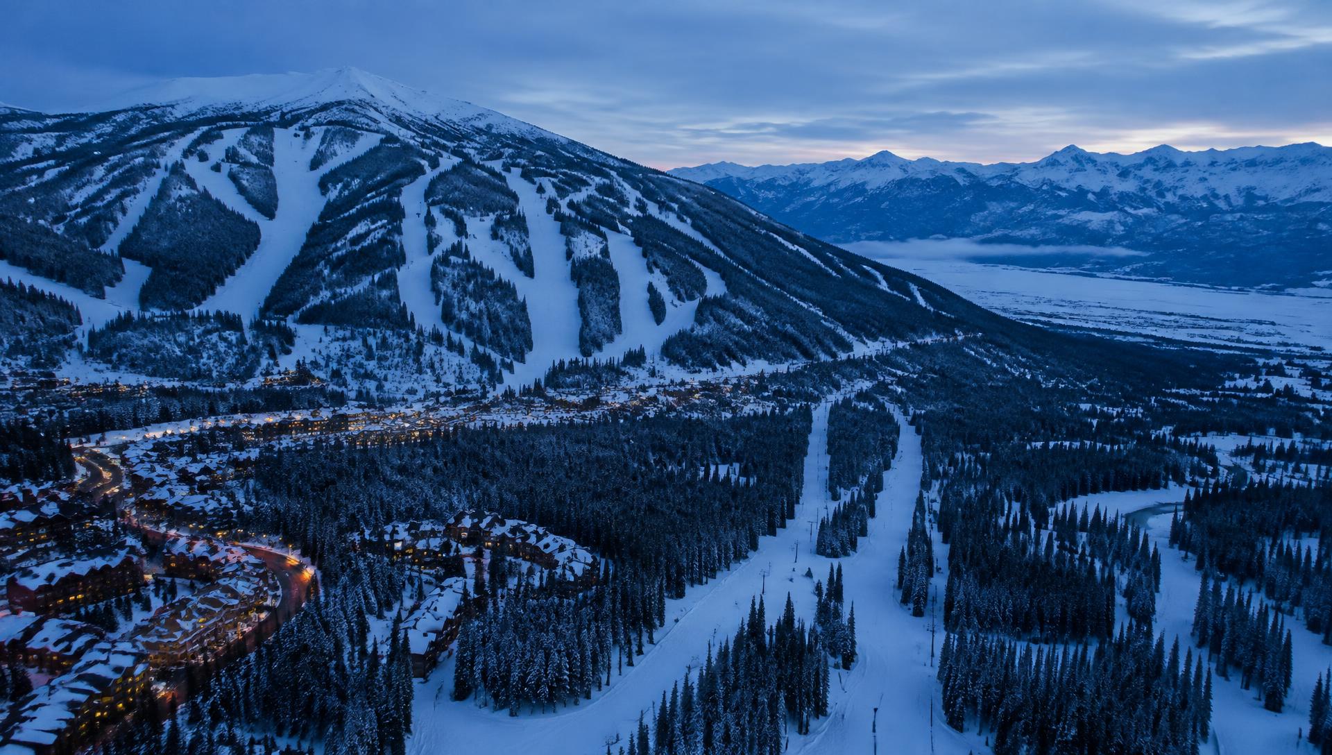 Aerial view of a snowy Montana mountain valley at blue hour with ski runs through evergreen forest