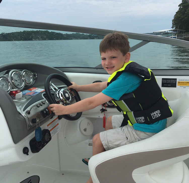 A young Collin Murphey at the helm of the boat in a life jacket