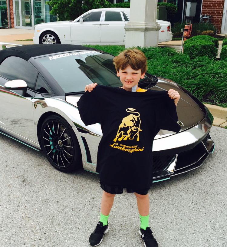 A young Collin Murphey holding a Lamborghini shirt in front of a chrome Lamborghini