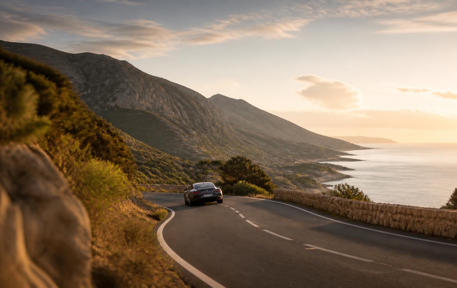 Performance grand touring car on a winding coastal road at golden hour