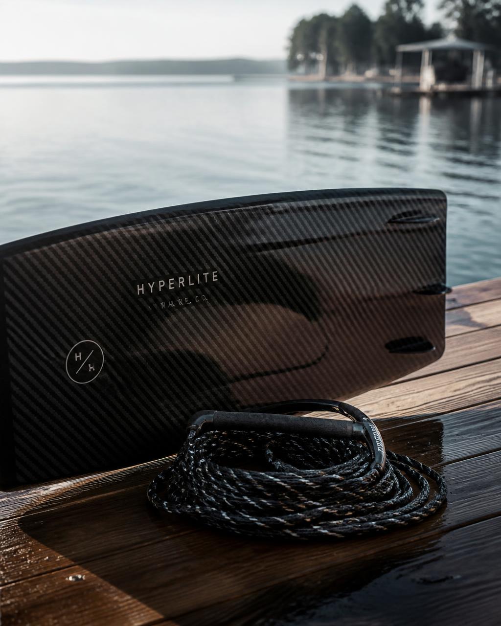 Carbon fiber wakeboard and rope coiled on a sunlit wooden dock