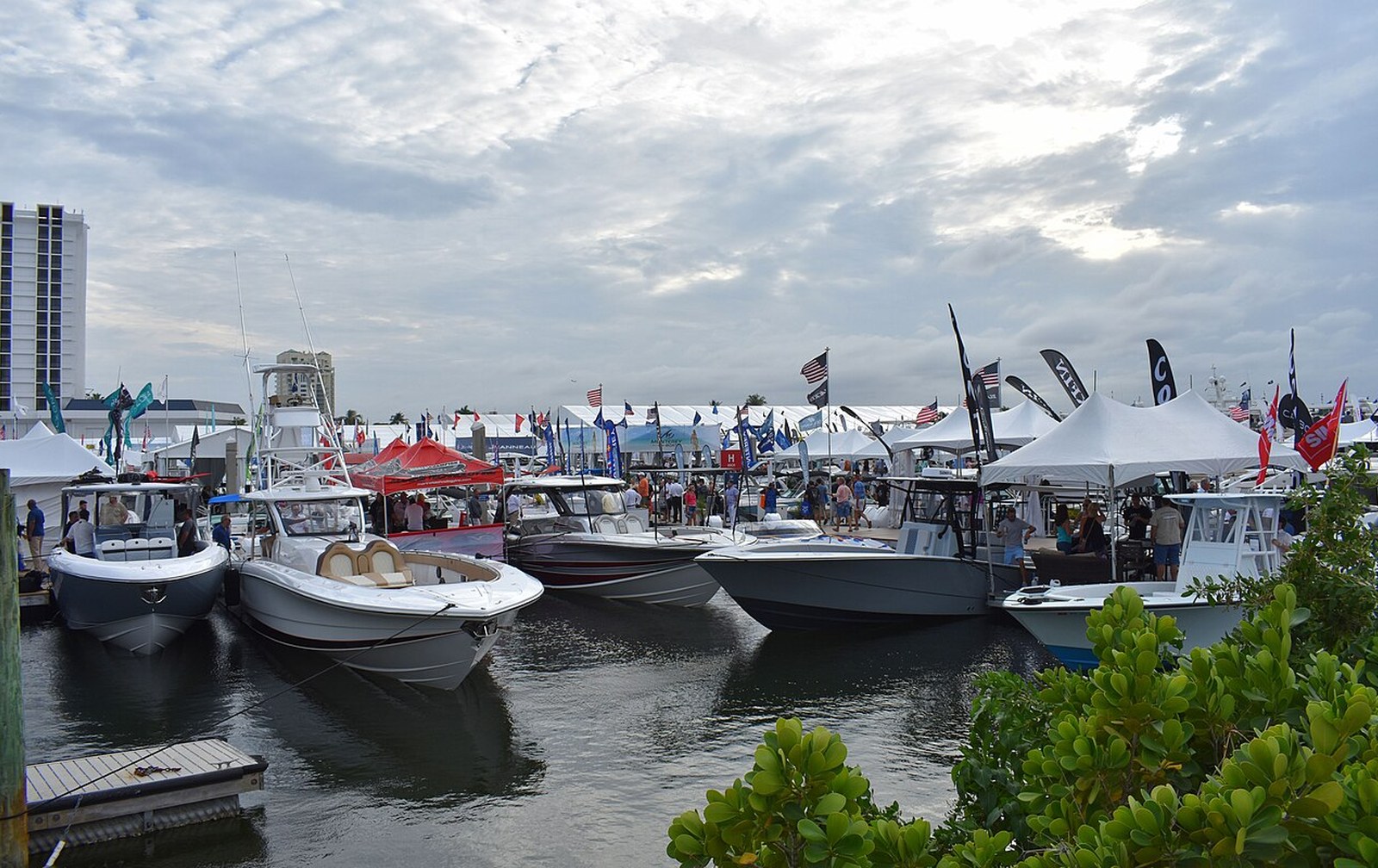 Rows of yachts along a floating show dock at golden hour with visitors walking between them