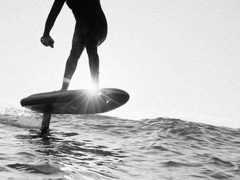 Rider lifted above the water on a Fliteboard hydrofoil, backlit by the sun
