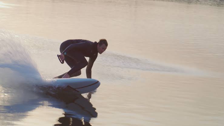 Rider carving a LIND electric surfboard across calm open water