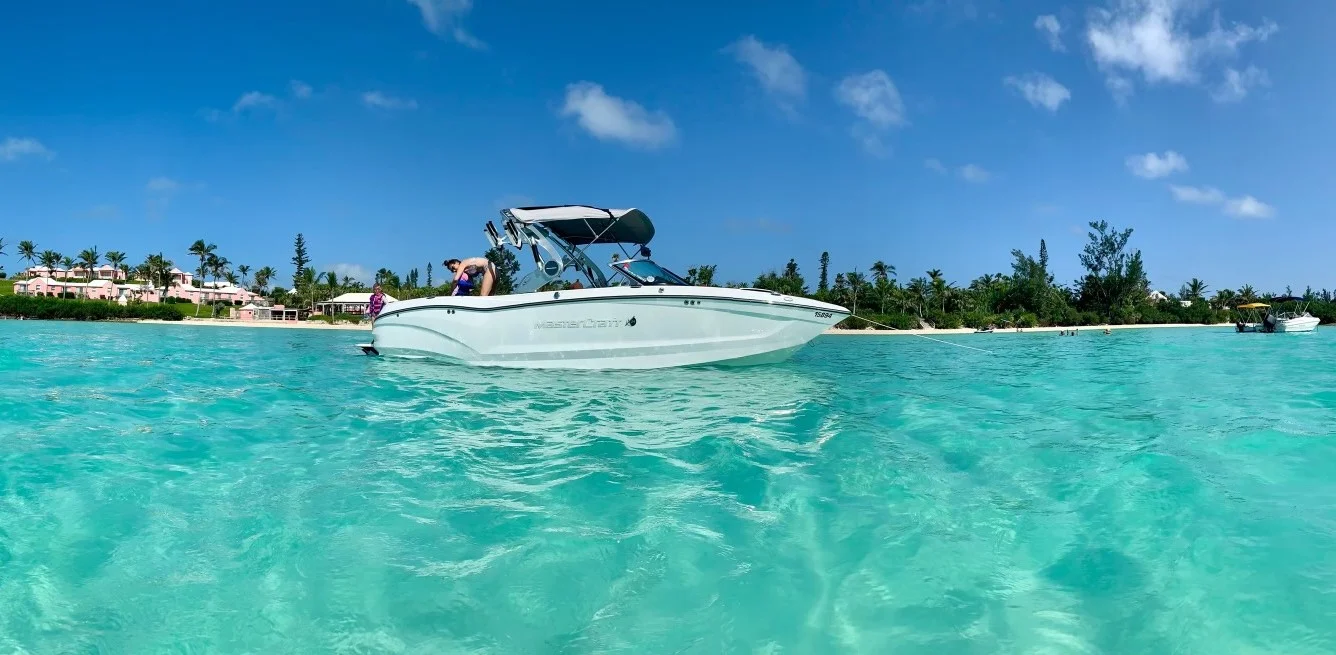White MasterCraft boat anchored in bright turquoise water with a tropical shoreline