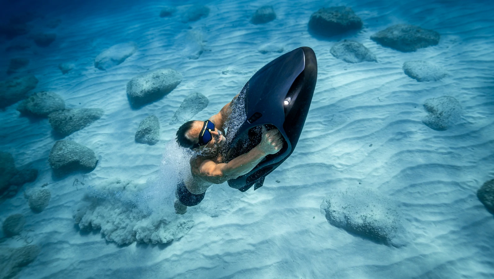 Rider steering a SEABOB underwater above a sandy seabed