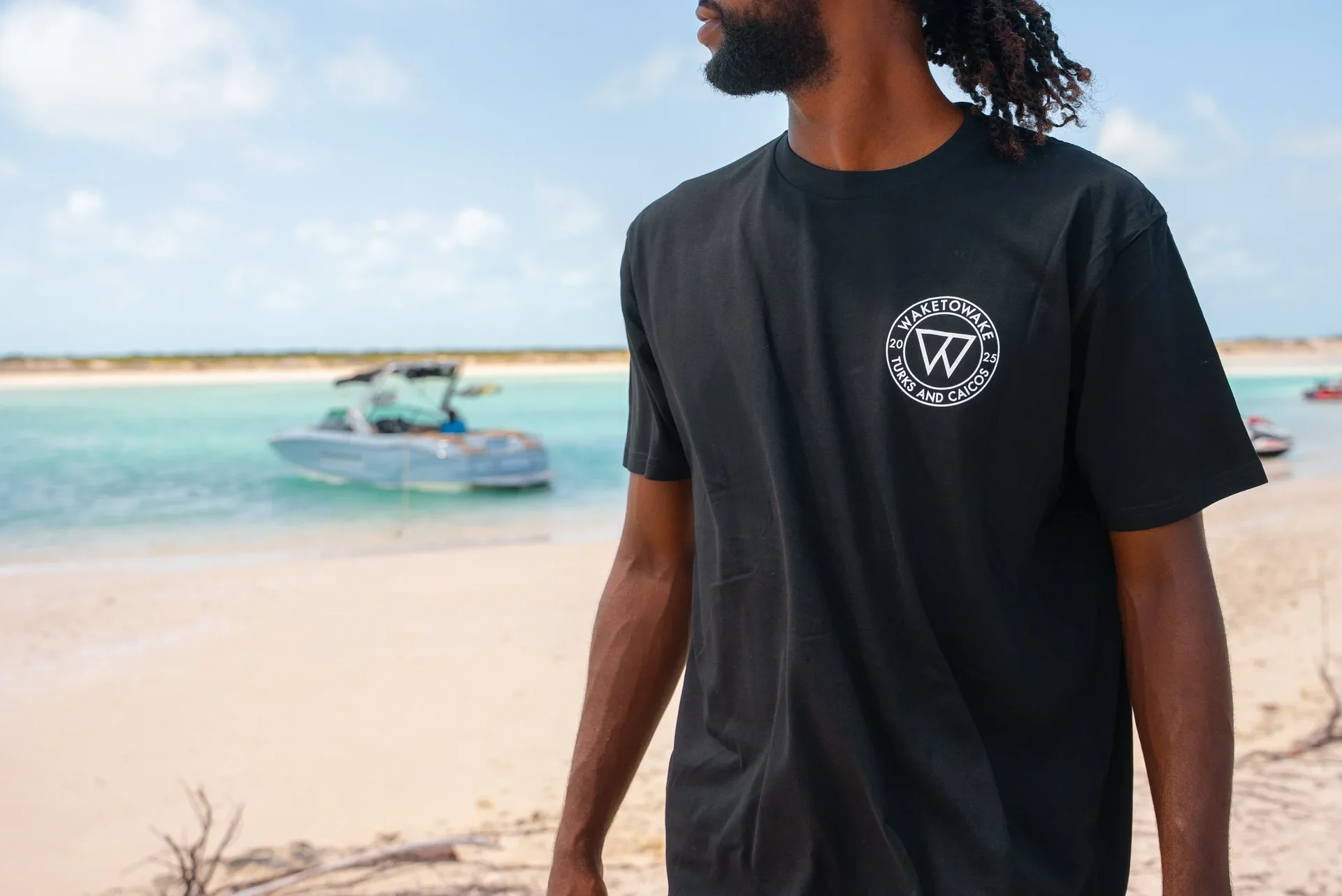 Wake to Wake team member on the beach with a boat anchored behind