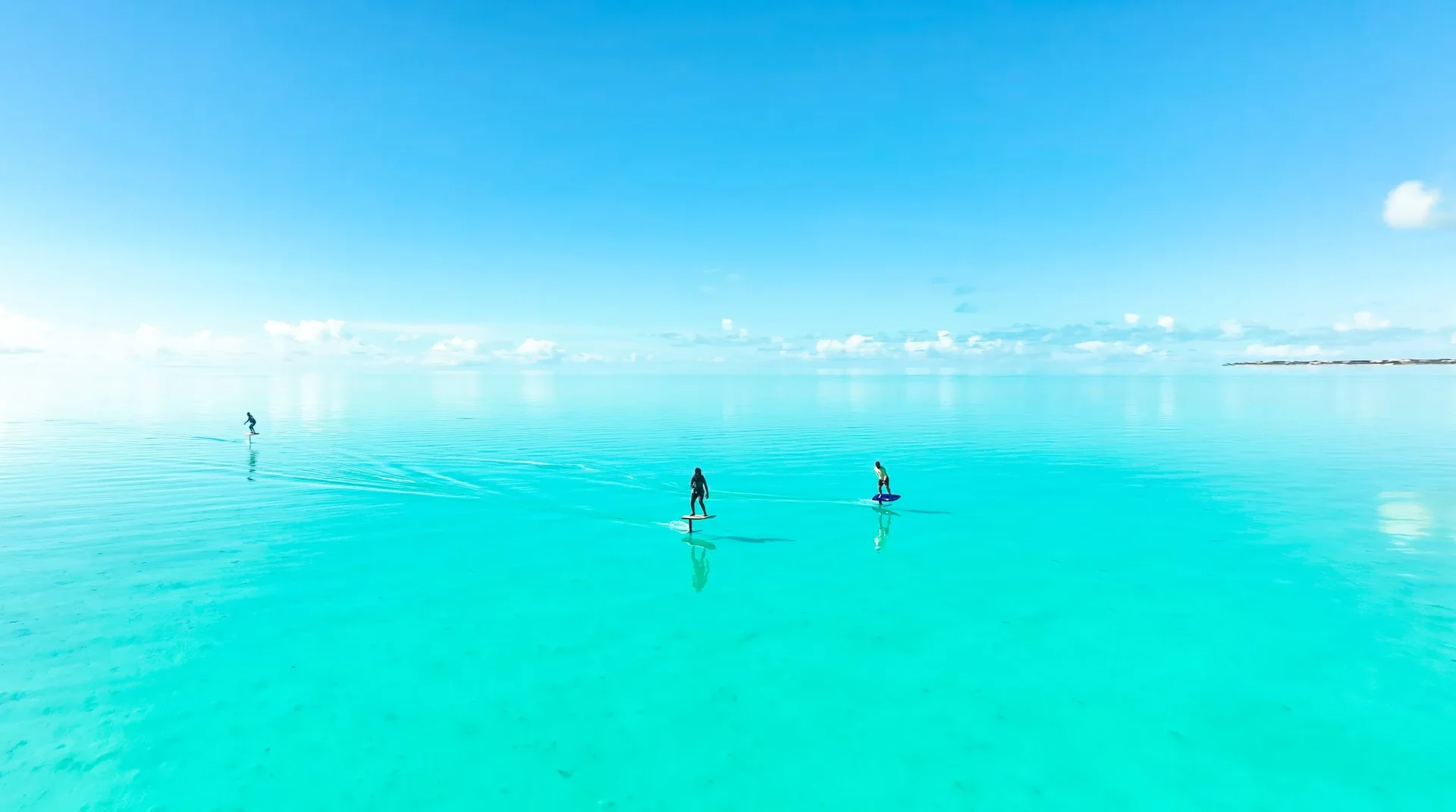 Two paddlers standing on boards across glassy turquoise flats