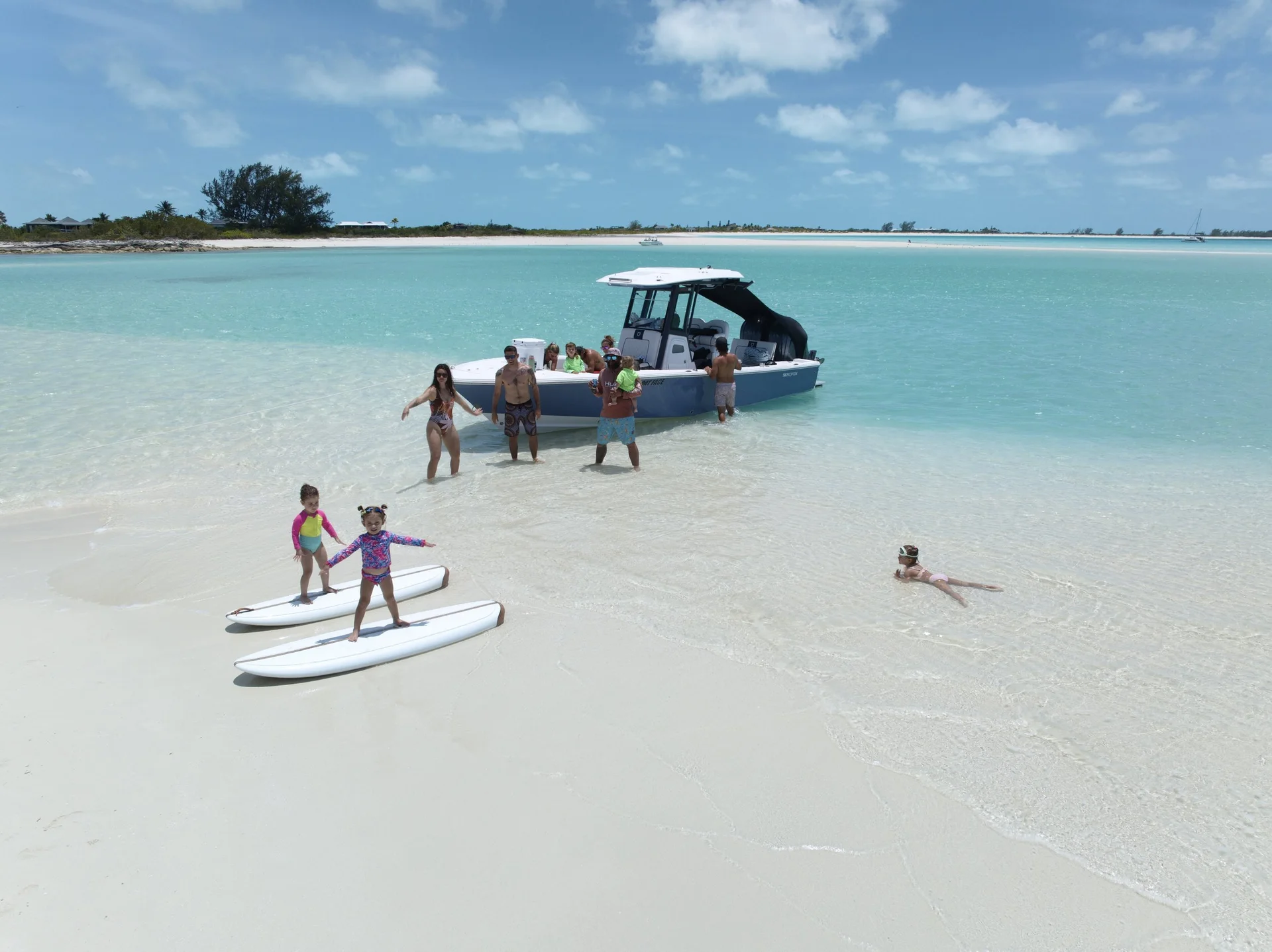 Group swimming and standing on a remote sandbar beside a Wake to Wake boat