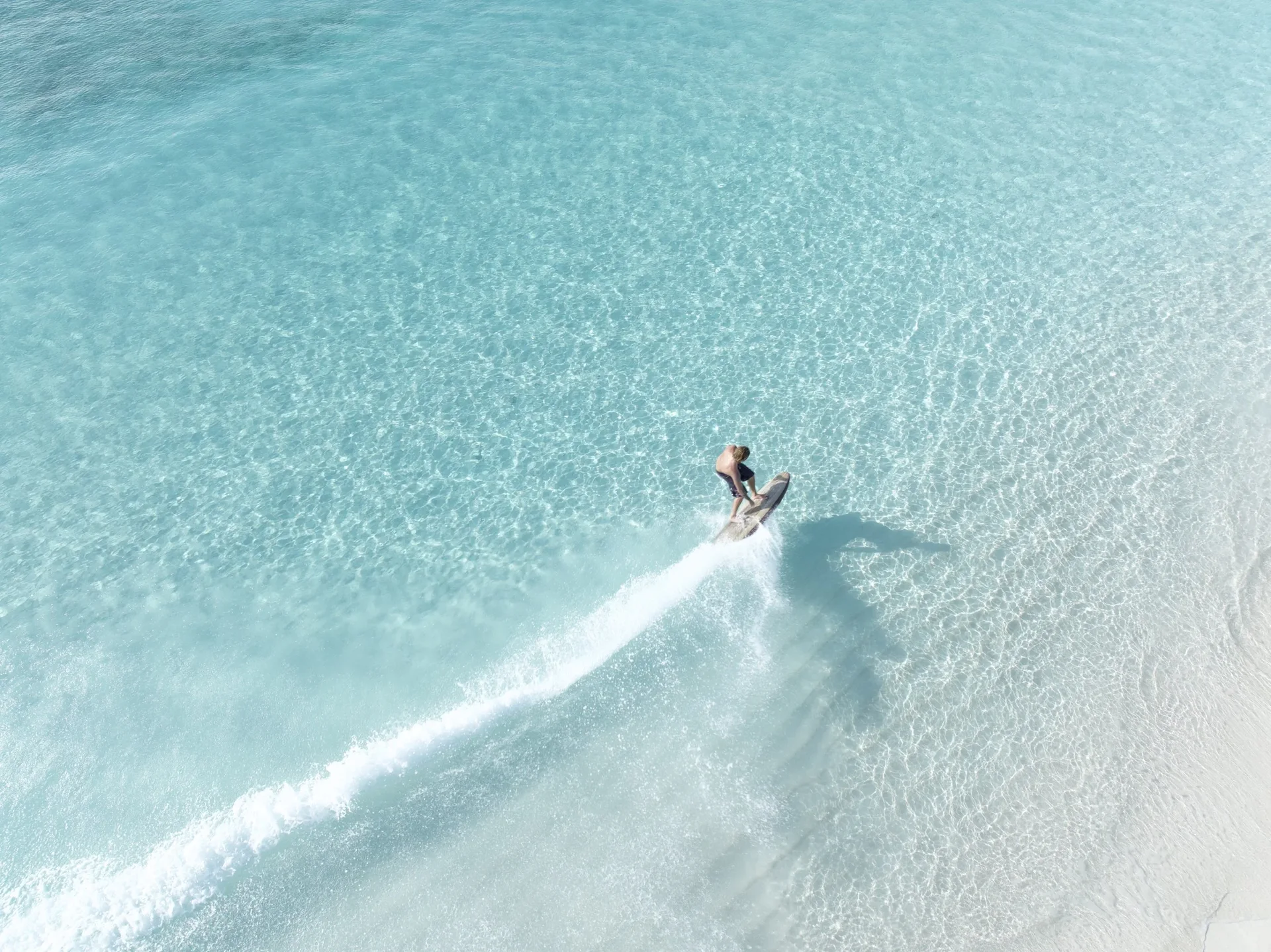 Aerial view of a rider carving a clean line across shallow turquoise water