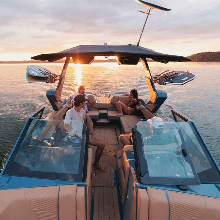 Friends relaxing on a wake boat at sunset with boards on the tower